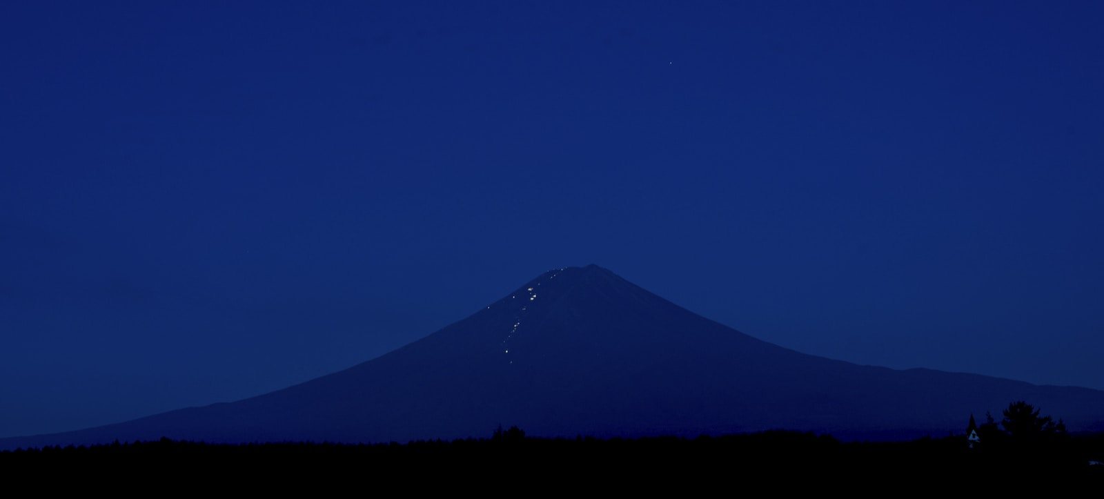夜明け前の富士山と登山道に連なるヘッドランプの光
