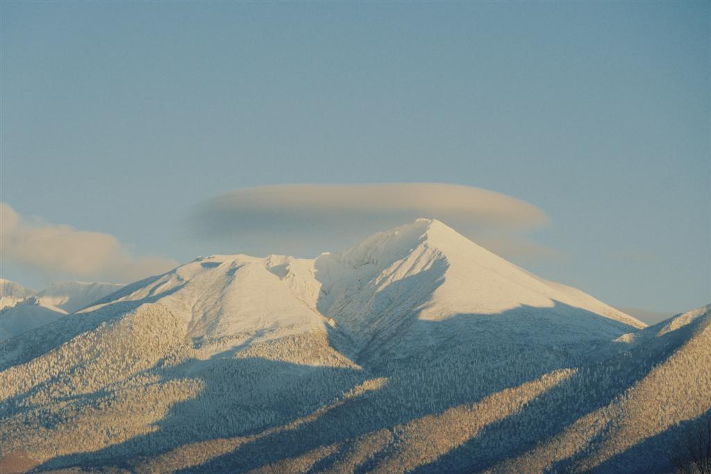 雪をかぶった山頂に笠のようにかかるレンズ雲