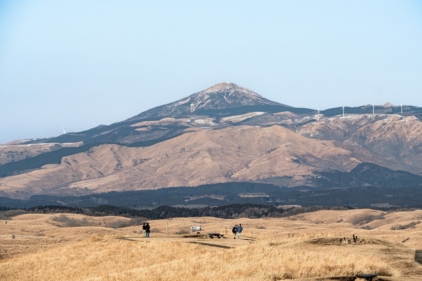 山を背にした枯れ草の高原を歩く人