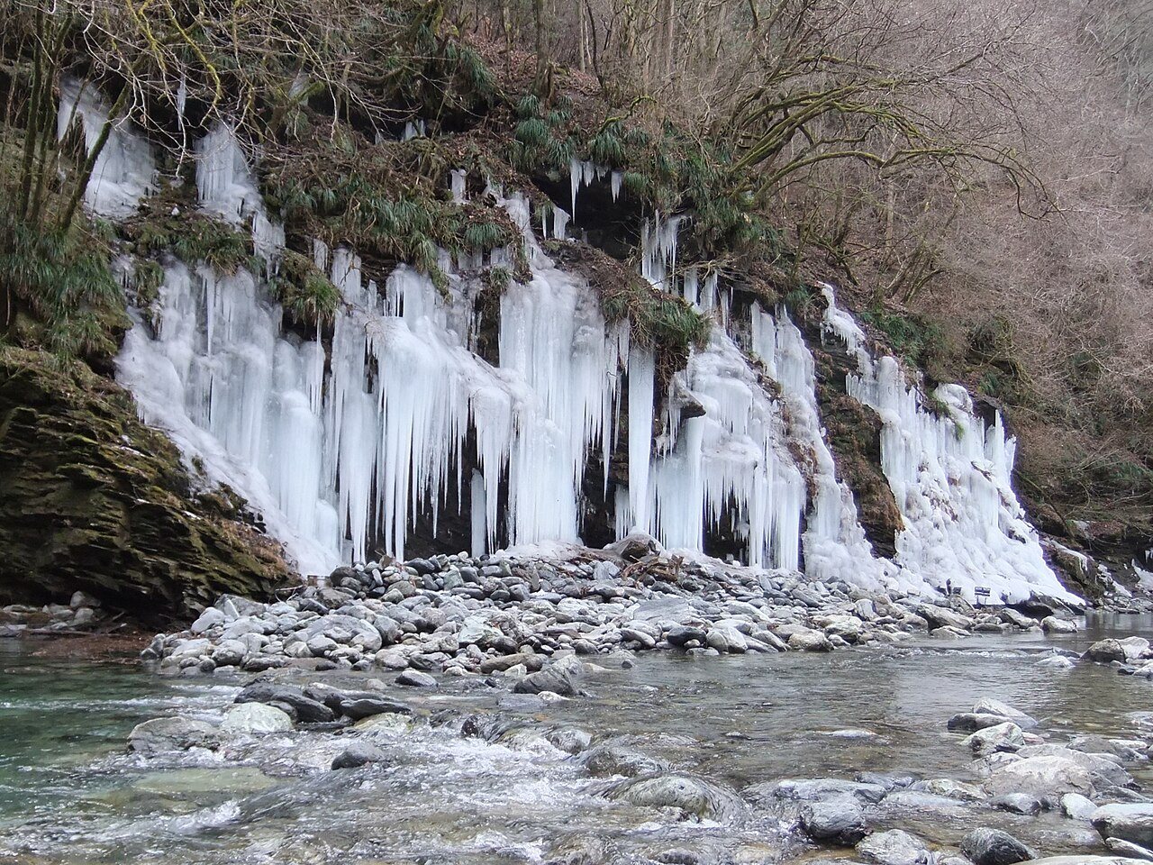 雪の残る河原の奥に並ぶ氷柱