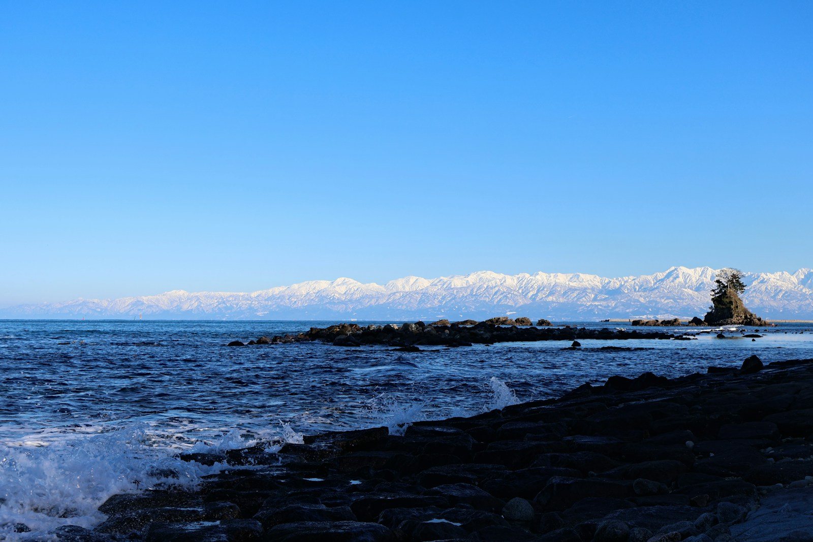 岩の多い海岸と沖の岩、遠くの雪山